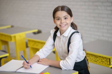 Okul üniformalı neşeli kız masada oturuyor.