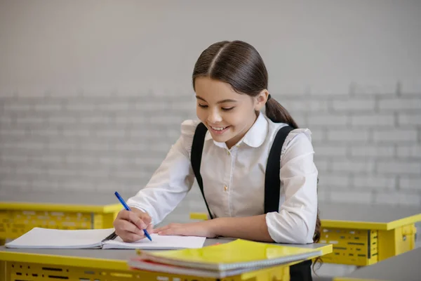 穿着校服的女孩在课桌边写字 — 图库照片