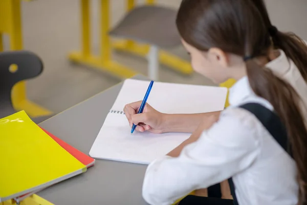 Chica escribiendo diligentemente en cuaderno en el escritorio —  Fotos de Stock