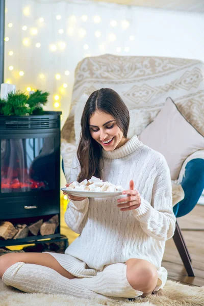 Женщина в белой одежде ест зефир и улыбается — стоковое фото