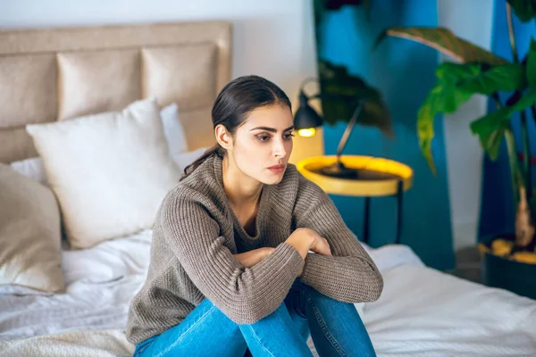 Mujer morena sentada en la cama y con aspecto frustrado —  Fotos de Stock