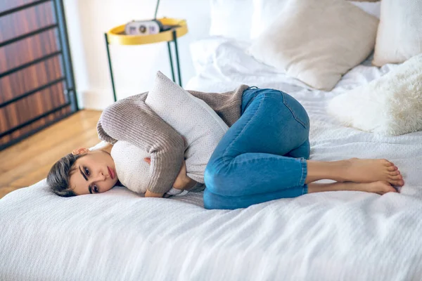 Темноволоса молода жінка лежить на ліжку і обіймає подушку — стокове фото