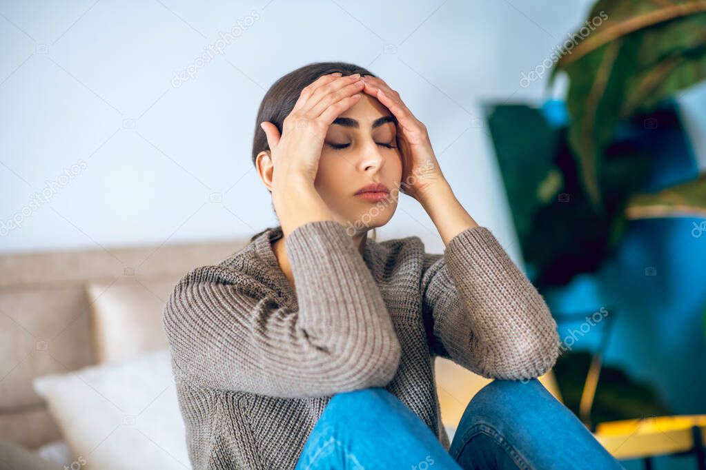Dark-haired woman sitting on bed and looking frustrated