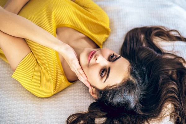 Длинноволосая красивая молодая женщина лежит на кровати и выглядит расслабленной — стоковое фото