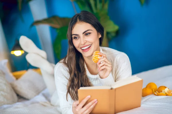 Mladá krásná žena čtení knihy a jíst mandarinky — Stock fotografie