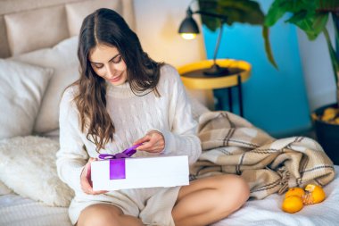 Koyu saçlı kadın elinde bir hediye tutuyor.