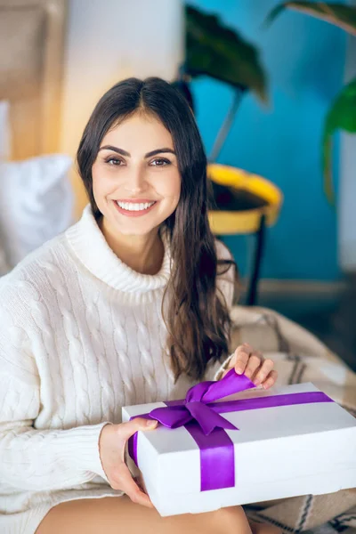 Donkerharige vrouw met een geschenk in haar handen en glimlachend — Stockfoto