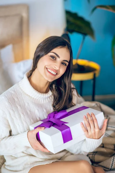 Donkerharige vrouw met een geschenk in haar handen en glimlachend — Stockfoto
