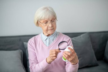 Senior woman with magnifier scrutinizing the medicines clipart
