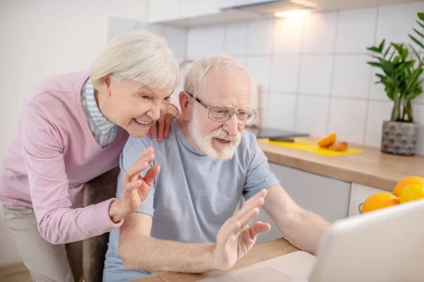 Pareja mayor teniendo una videollamada y mirando contenta — Foto de Stock