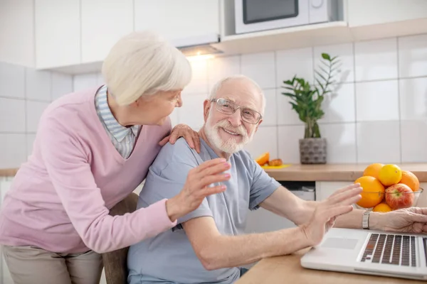 Pareja mayor teniendo una videollamada y mirando contenta — Foto de Stock