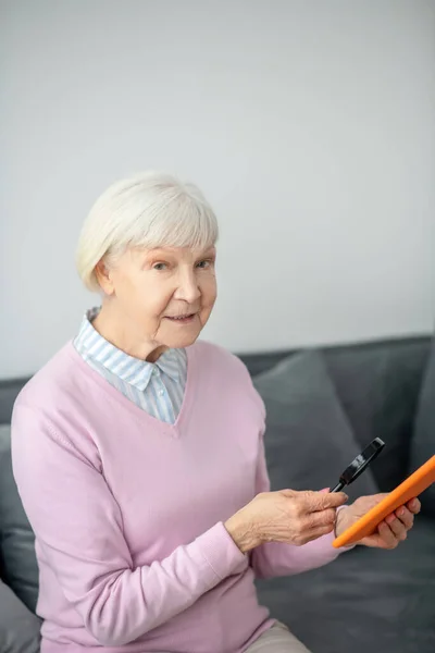 Donna anziana con lente di ingrandimento guardando qualcosa su un tablet — Foto Stock