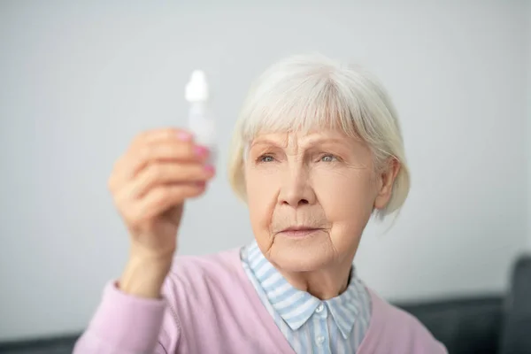 Старшая женщина держит бутылку с глазными капельками — стоковое фото