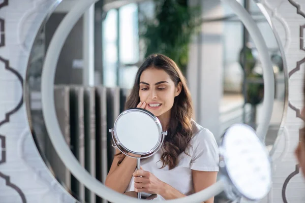 Mujer mirando el pequeño espejo en su baño — Foto de Stock