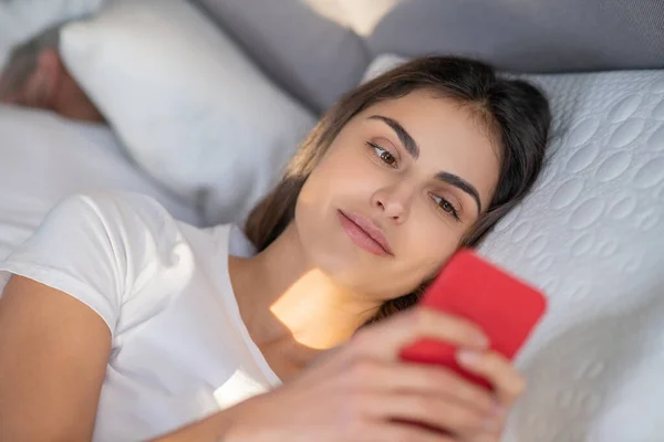 Kvinna som använder en smartphone i en säng — Stockfoto