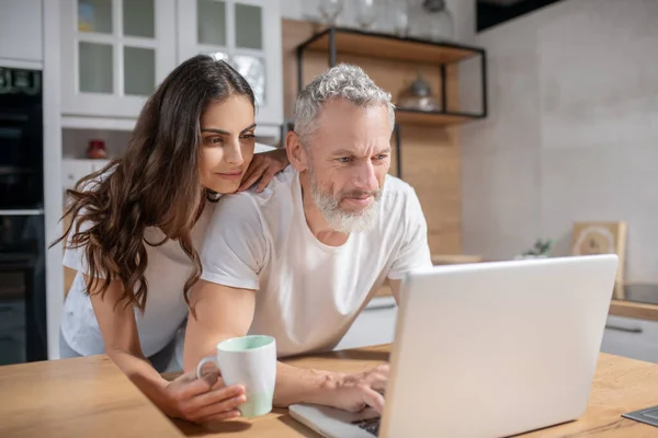 Mulher abraçando seu marido enquanto ele está verificando e-mails — Fotografia de Stock