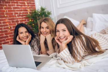 Üç kız yatağa uzanıp dizüstü bilgisayarda bir şeyler izliyorlar.
