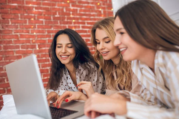 Tres chicas tumbadas en la cama y viendo algo en un portátil — Foto de Stock