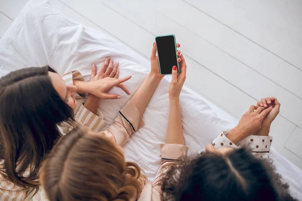 Gadis dengan smartphone berbaring di tempat tidur dan menonton sesuatu — Stok Foto