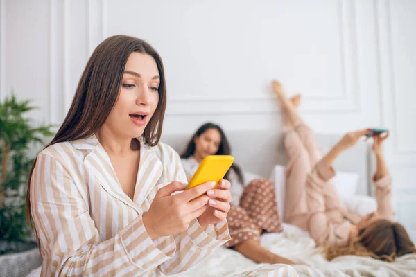 Gadis dengan smartphone berbaring di tempat tidur dengan smartphone dan tampak terlibat — Stok Foto