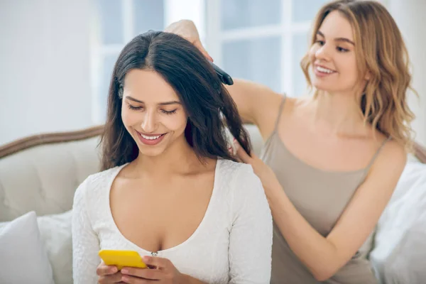 Blondes hübsches Mädchen macht ihrer lächelnden Freundin Haare — Stockfoto