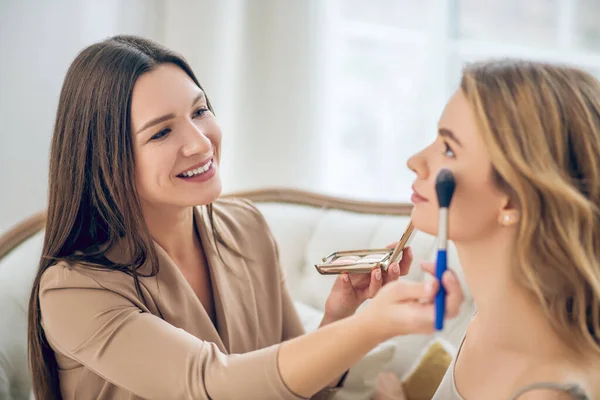 Morena sonriente chica haciendo maquillaje a su amigo — Foto de Stock