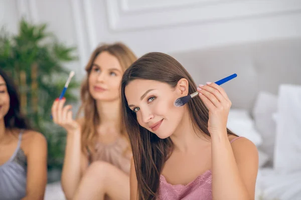 Morena sonriente chica sosteniendo un cepillo y haciendo maquillaje — Foto de Stock