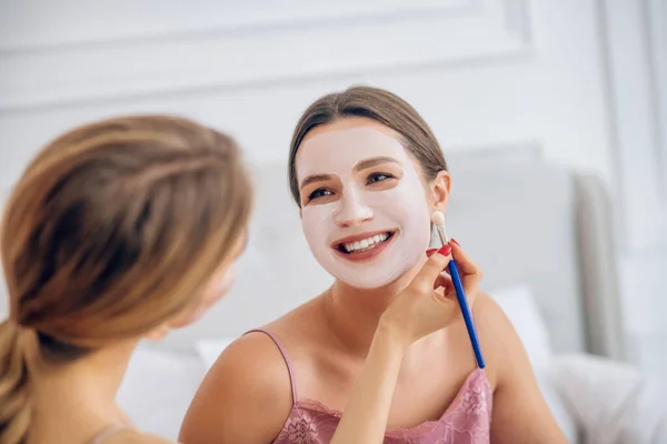 Chica rubia aplicando máscara facial en su cara de amigos sonrientes — Foto de Stock