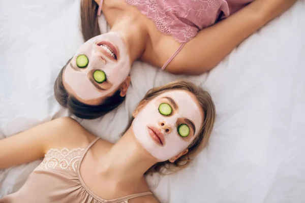 Dua gadis berbaring di tempat tidur dengan masker wajah di wajah mereka — Stok Foto