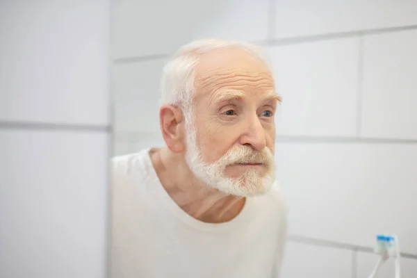 Homem de cabelos grisalhos em tshirt branca olhando no espelho — Fotografia de Stock