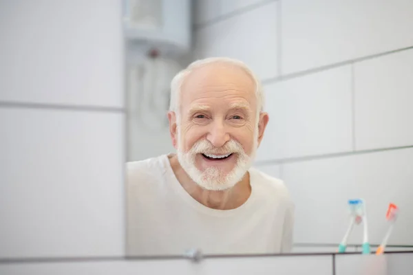 Γκρι μαλλιά άντρας με λευκό μπλουζάκι κοιτάζοντας στον καθρέφτη — Φωτογραφία Αρχείου