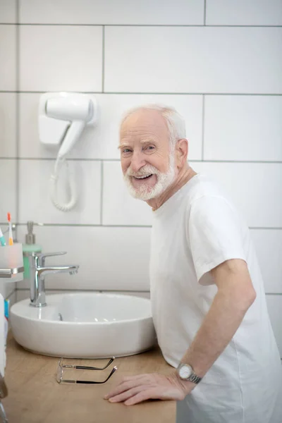 Le gråhårig man i vit tröja i badrummet — Stockfoto