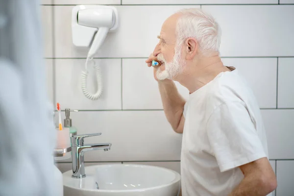 Šedovlasý muž v bílém tričku si čistí zuby — Stock fotografie