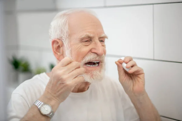 Hombre canoso en camiseta blanca limpiando dientes con hilo dental —  Fotos de Stock