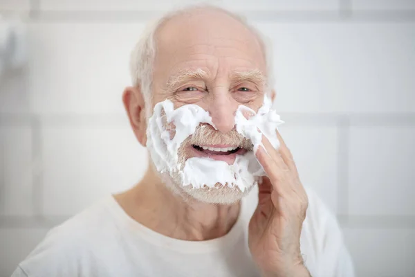 Gray-haired man in white tshirt shaving in the bathroom — Stock Photo, Image