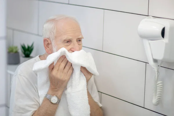 Grijsharige man in wit shirt veegt zijn gezicht af met de handdoek — Stockfoto