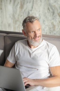 Yatakta dizüstü bilgisayarı olan bir adam var.