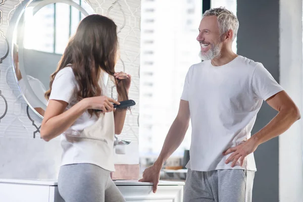 Hombre y mujer alegres peinando de pie cerca del espejo — Foto de Stock