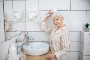 Saçlarını banyoda kurutan gri saçlı kadın.