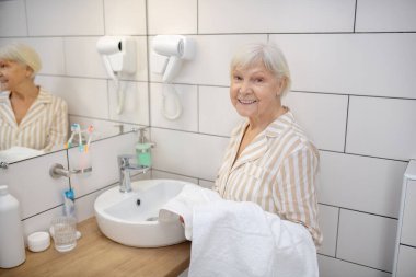Banyoda elinde havluyla beyaz saçlı bir kadın.
