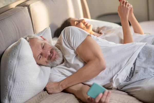 Férfi és nő okostelefonnal feküdt az ágyon — Stock Fotó