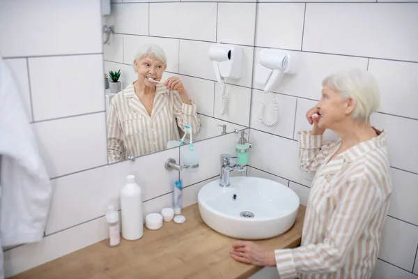 Oudere vrouw poetsen haar tanden in de badkamer — Stockfoto