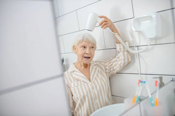 Saçlarını banyoda kurutan gri saçlı kadın. — Stok fotoğraf
