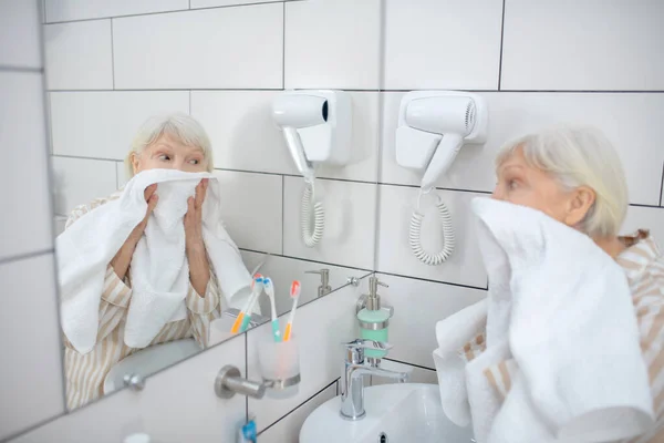 Grauhaarige Frau trocknet ihr Gesicht mit dem Handtuch — Stockfoto