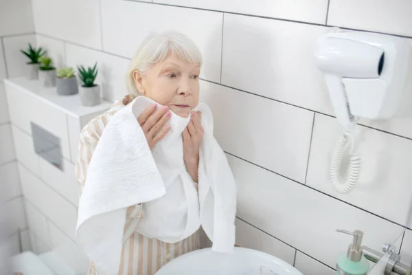 Gråhårig kvinna torkar ansiktet med handduken — Stockfoto