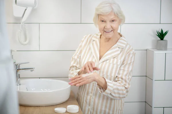 Starší usměvavá žena nanáší krém na ruce — Stock fotografie