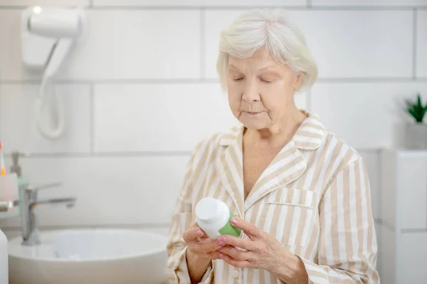 Vieja de pelo corto sosteniendo una botella con vitaminas en las manos — Foto de Stock