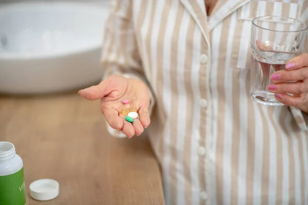 Woman in pajama holding a pills in her hands and a glass of water — Stock Photo, Image