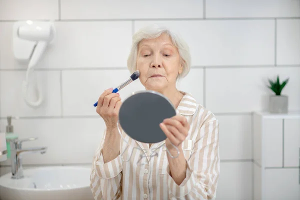 Mujer de pelo gris en pijama haciendo maquillaje en el baño —  Fotos de Stock