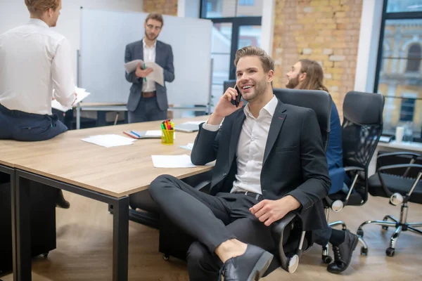 Man med smartphone i fåtölj och kommunicerande kollegor — Stockfoto